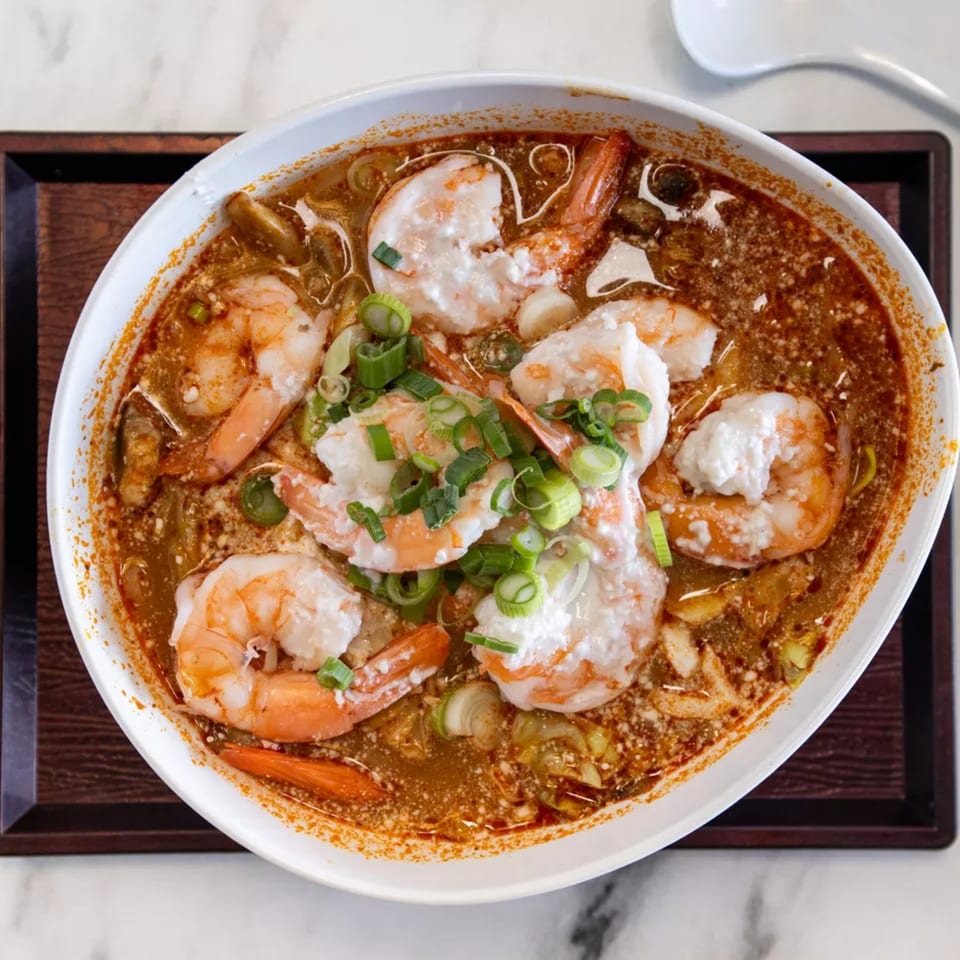 Overhead view of a bowl of spicy Thai Tom Yum soup with shrimp and green onions.