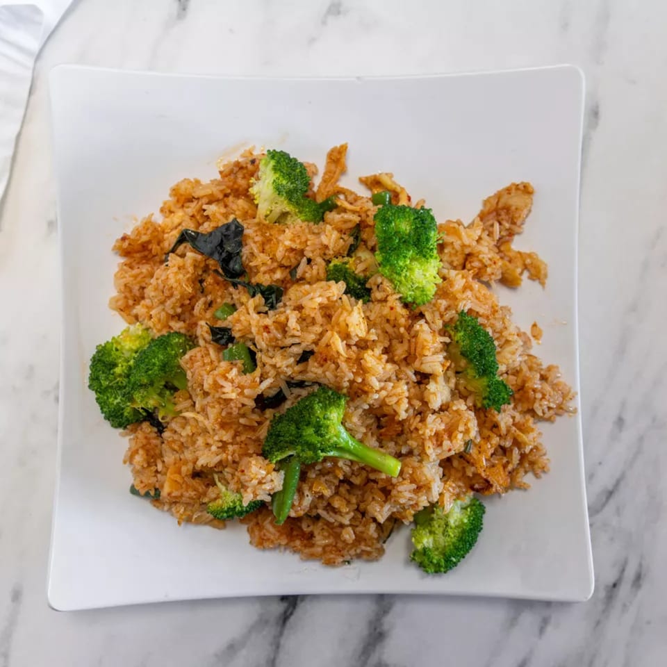 Spicy fried rice with broccoli florets and dark green herbs on a white square plate.