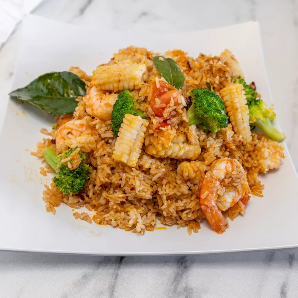 Seafood fried rice with shrimp, squid, broccoli, and baby corn on a white plate.