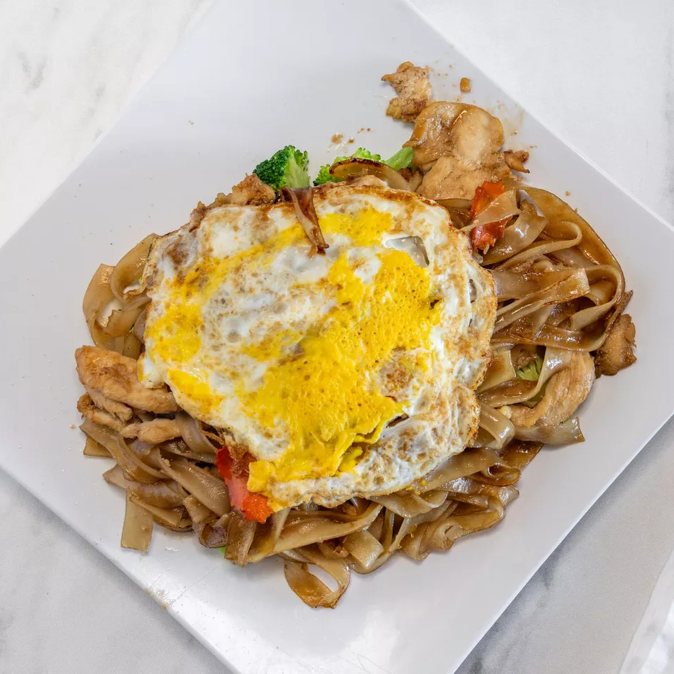 Pad Thai with chicken, broccoli, red peppers, and a fried egg on a white plate.