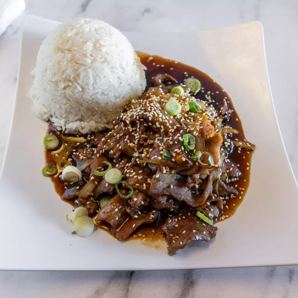 Beef teriyaki with white rice, sesame seeds, and green onions on a white plate.
