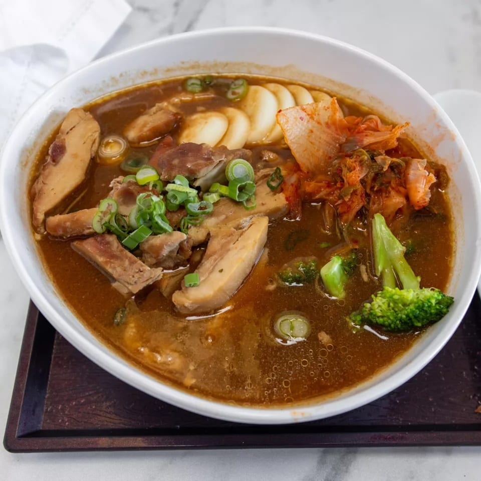 A bowl of Pad Thai Café's ramen with chicken, kimchi, broccoli, and scallions in a rich broth.