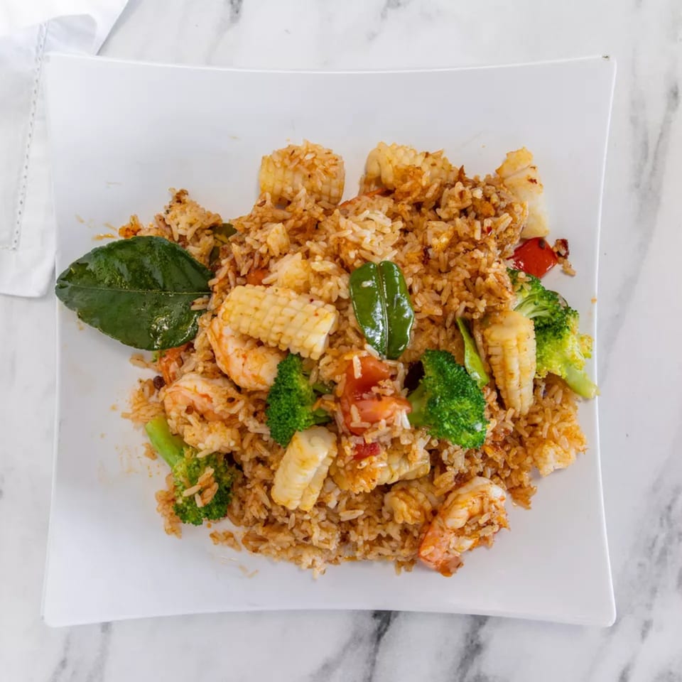 Seafood fried rice with shrimp, squid, broccoli, baby corn, and red peppers on a white plate.