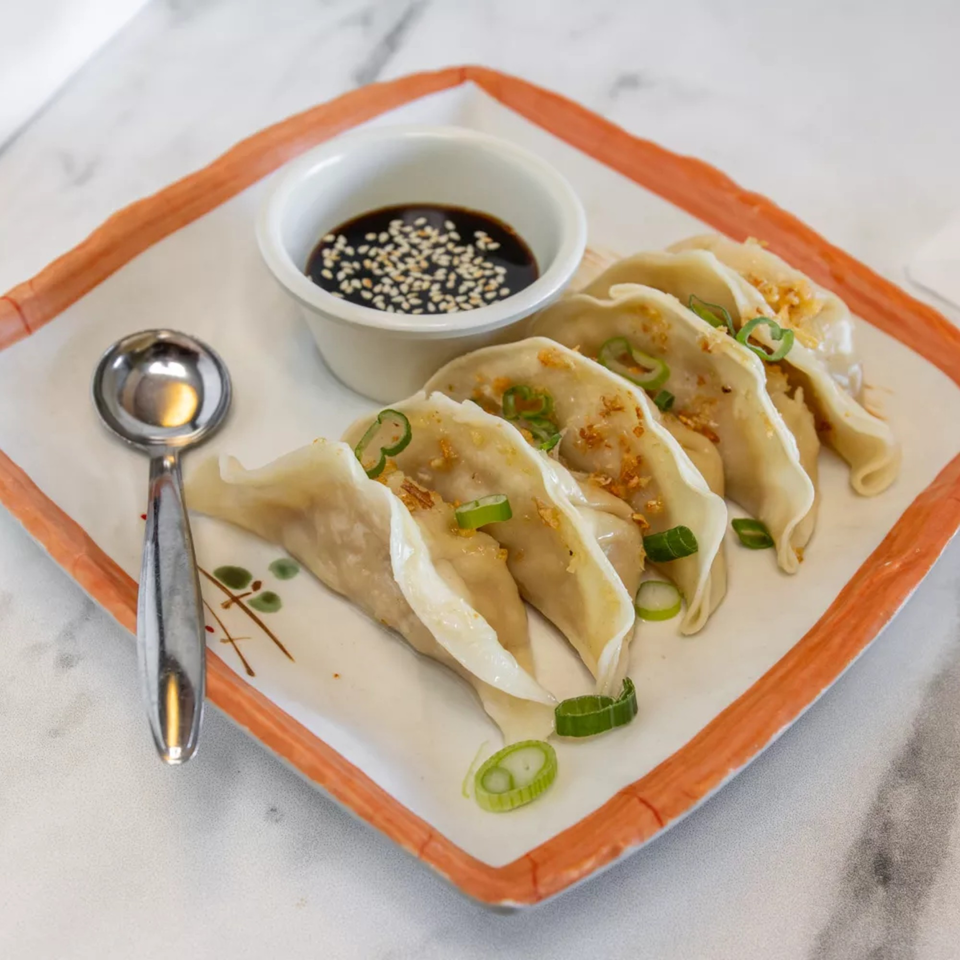 Five Thai dumplings with fried garlic and green onions, served with soy sauce and a spoon.