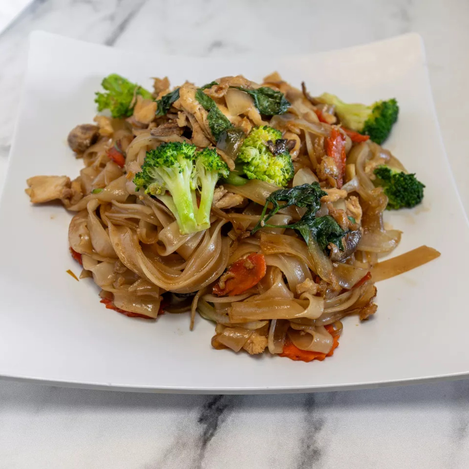 Pad See Ew with wide rice noodles, chicken, broccoli, and carrots on a white plate.