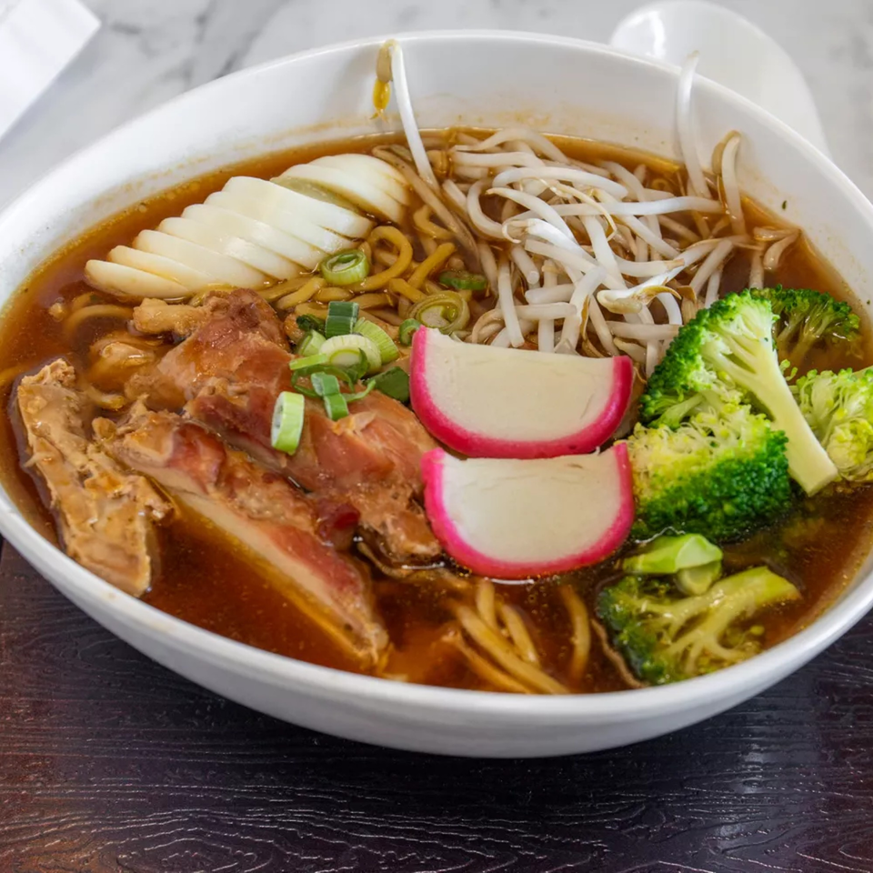 A bowl of Thai ramen with chicken, sliced eggs, bean sprouts, broccoli, and fish cakes.