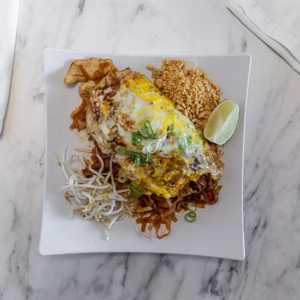 Pad Thai noodles with a fried egg, bean sprouts, crushed peanuts, and a lime wedge.